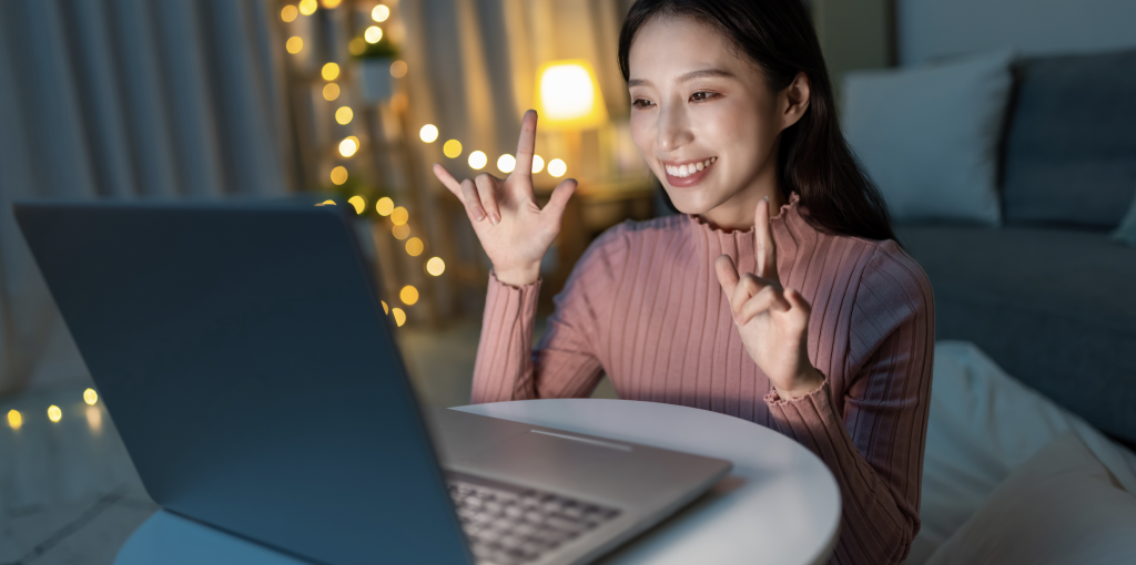 A woman signs two ASL ILY Handshape to a laptop screen using Sign Language Blitz.