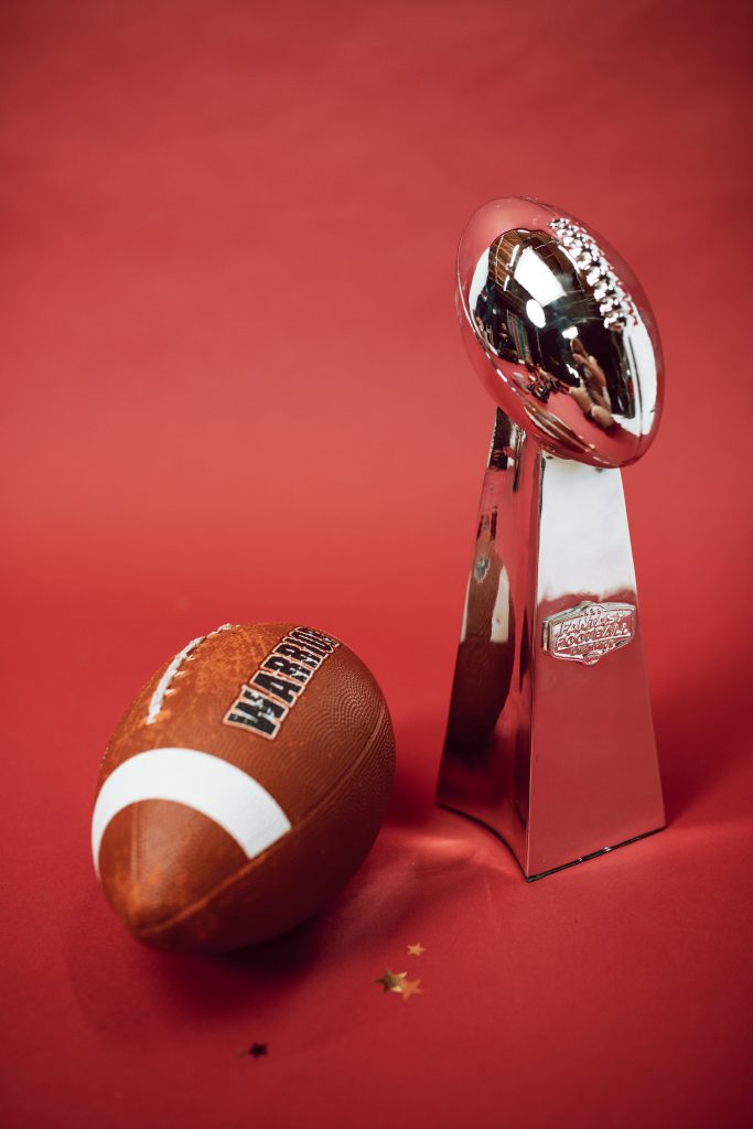 A trophy with a football on it sits next to a football with a red background.
