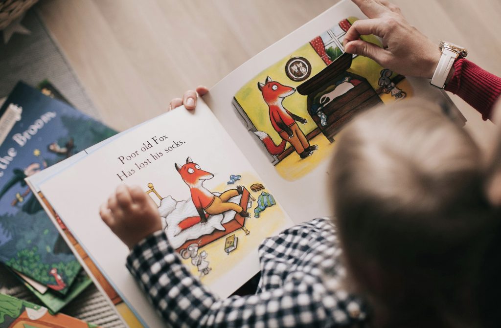 A child is reading a book. The page has a fox sitting on a bed.