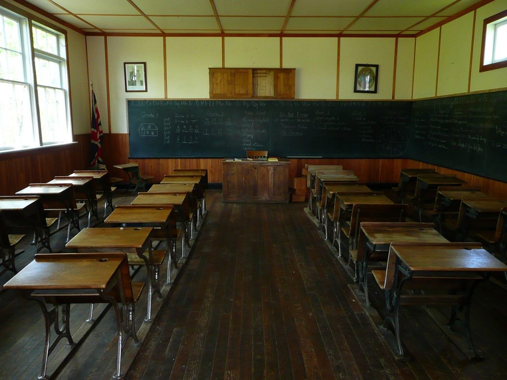 Inside of an old school house with a chalkboard and old desks.